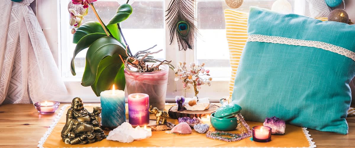 Okno s polštářem, svíčkami, rostlinou, soškou Buddhy a krystaly na parapetu