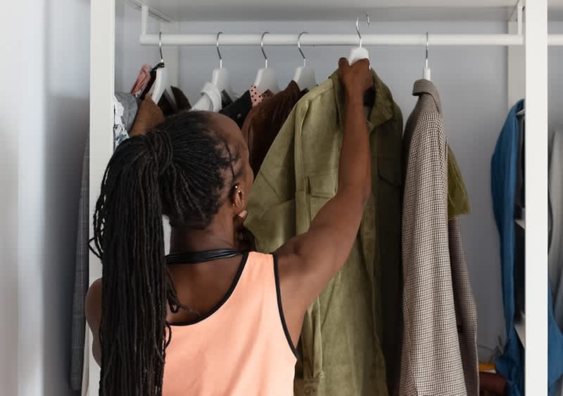 Žena vybírá oblečení ze skříně plné různých kabátů a bund.