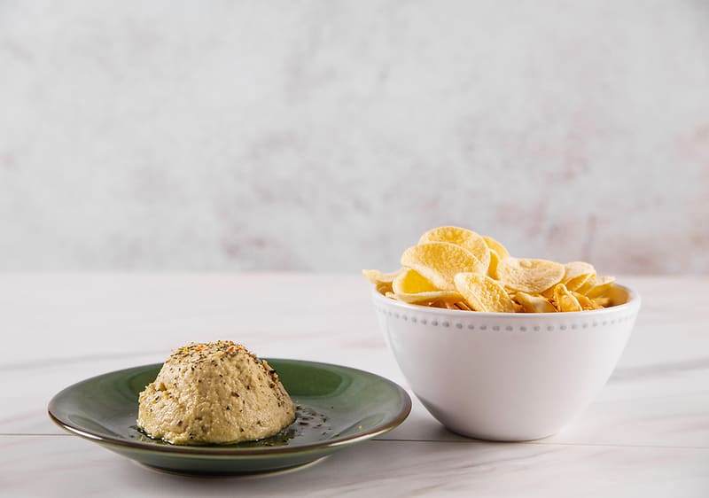 Hummus na talíři a chipsy v misce na světlém pozadí