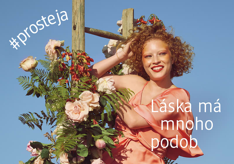 Žena v růžových šatech u květinové dekorace na modrém pozadí