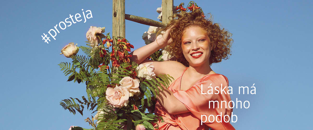 Žena v růžových šatech u květinové dekorace na modrém pozadí