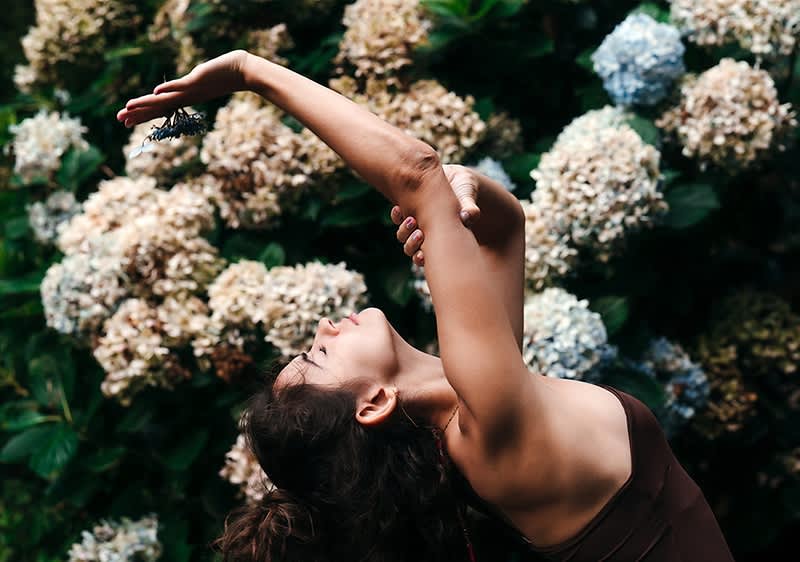 Žena cvičící jógu před keři s květy hortenzie