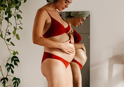 Těhotná žena stojí před zrcadlem