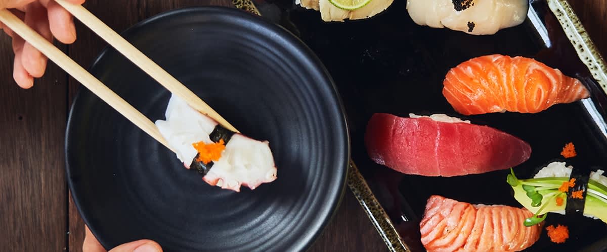 Sushi s chobotnicí držené hůlkami nad černým talířem