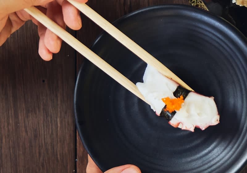 Sushi s chobotnicí držené hůlkami nad černým talířem