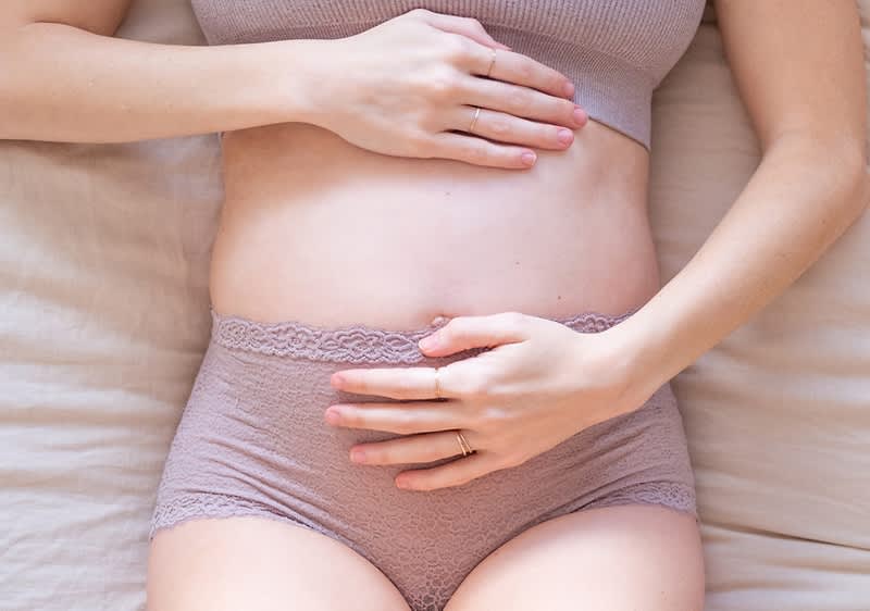 Těhotná žena ležící na posteli s rukama na břiše