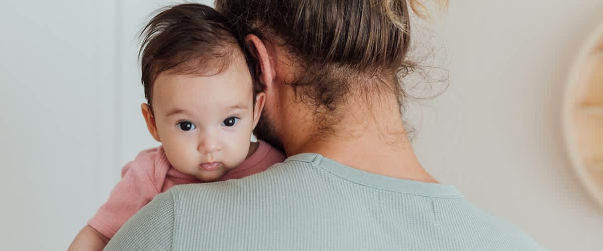 Máma drží dítě na rameni, oba mají hnědé vlasy.