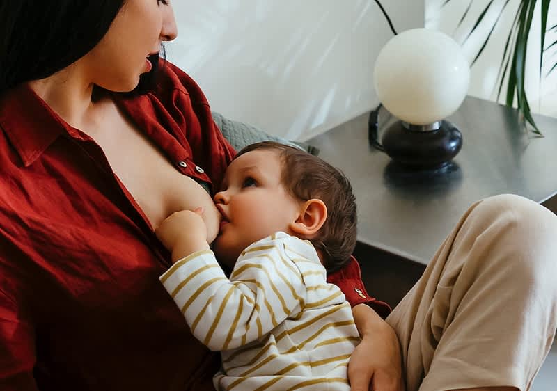 Žena kojící dítě na pohovce, vedle stolní lampa