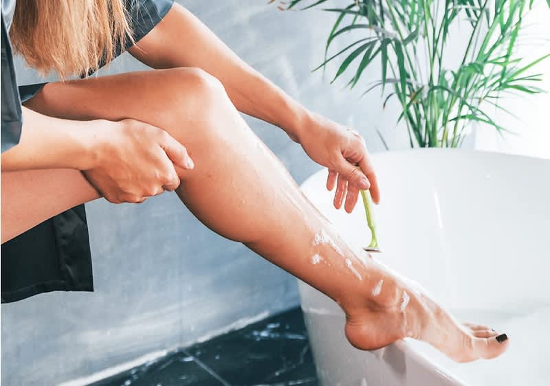 Žena si holí nohy nad vanou