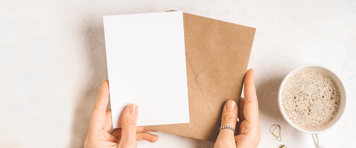 Ruce držící bílý papír a hnědou obálku