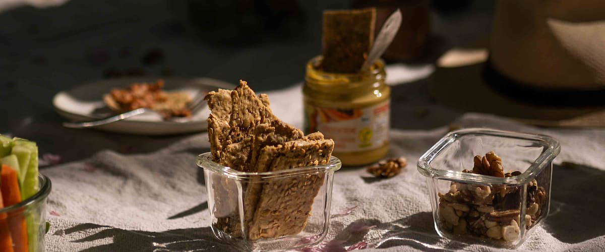 Piknikový stůl s krekry, ořechy, hořčicí a kloboukem na bílém ubrusu