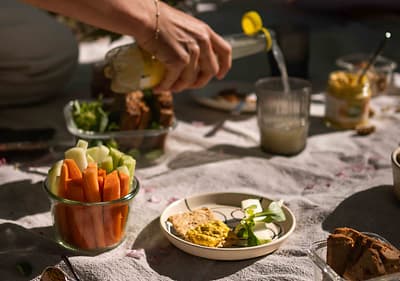 Piknikový stůl s čerstvou zeleninou, pomazánkou, chlebem a nalévaným nápojem