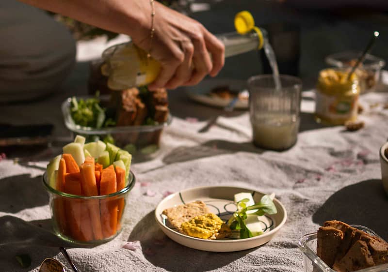 Piknikový stůl s čerstvou zeleninou, pomazánkou, chlebem a nalévaným nápojem