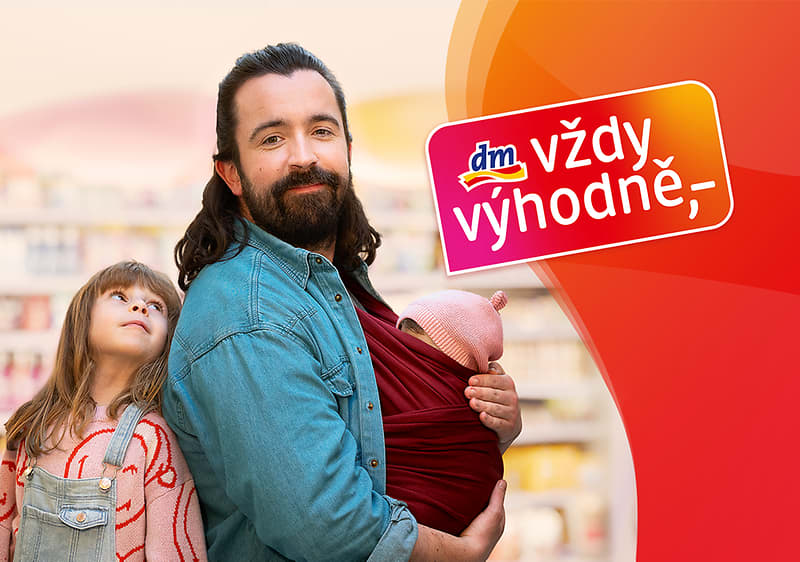 Muž s dítětem v šátku v obchodě, vedle dítě, logo dm vždy výhodně
