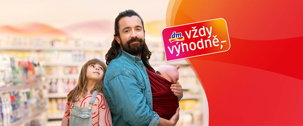 Muž s dítětem v šátku v obchodě, vedle dítě, logo dm vždy výhodně