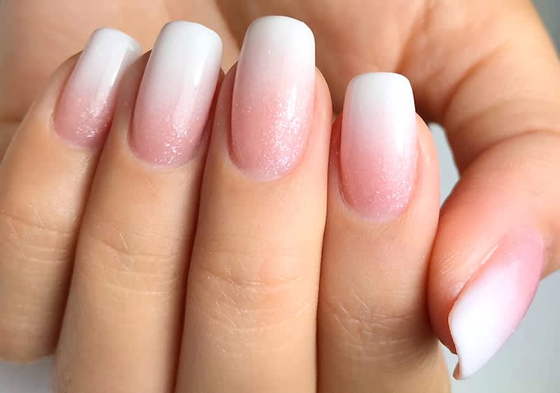 Francouzská manikúra s jemným růžovým a bílým gradientem na nehtech ruky.