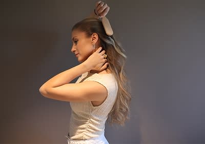 Žena s dlouhými blond vlasy si upravuje vlasy kartáčem