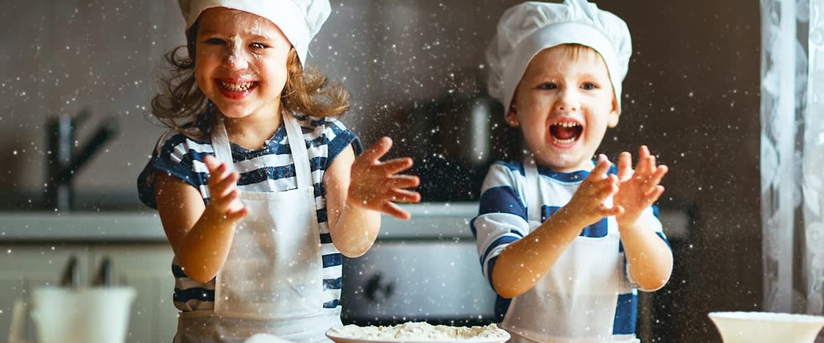 Děti v kuchařských čepicích házejí mouku v kuchyni