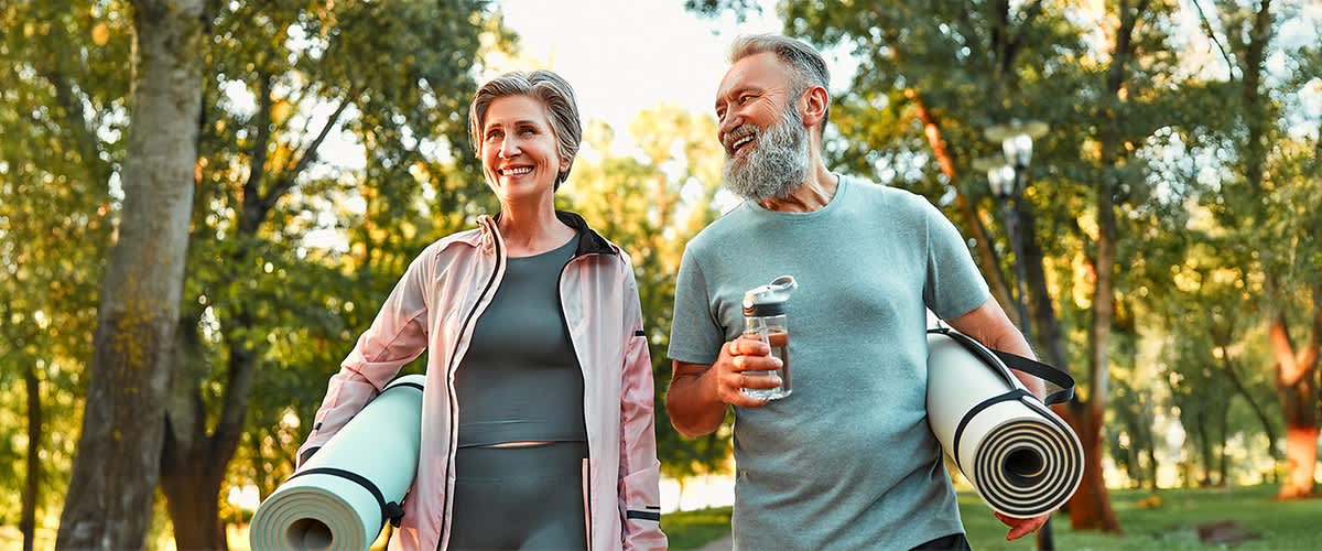 Žena a muž s podložkami na cvičení a lahví na vodu v parku