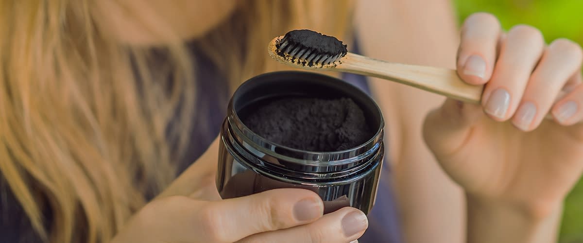 Žena drží kartáček s aktivním uhlím nad otevřenou nádobou
