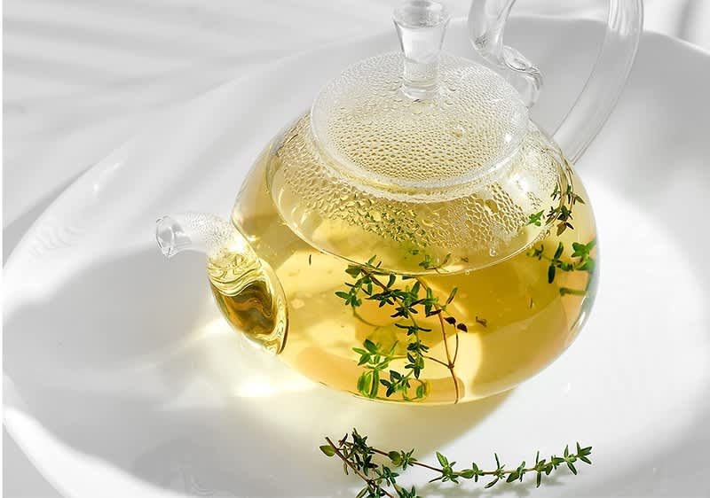 Skleněná konvice s bylinkovým čajem na bílém talíři