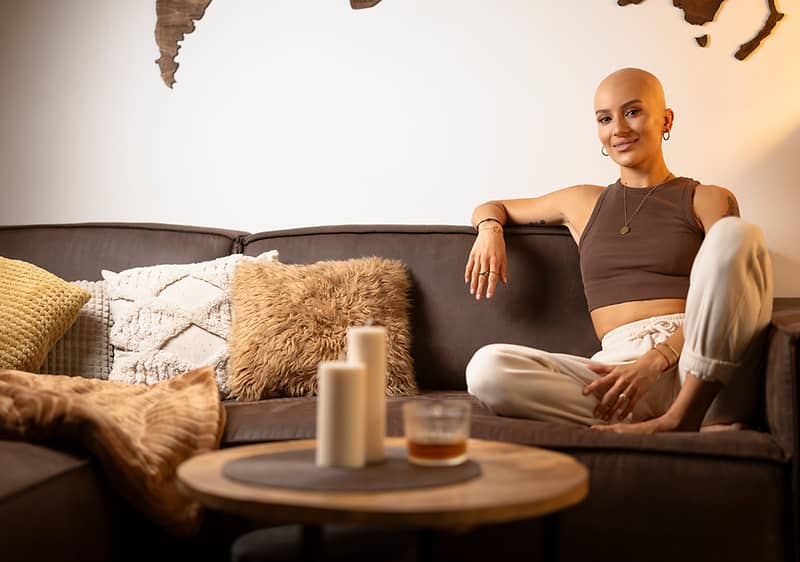 Osoba sedící na pohovce, svíčky na stole, polštáře a kožešina na pohovce, mapa světa na zdi