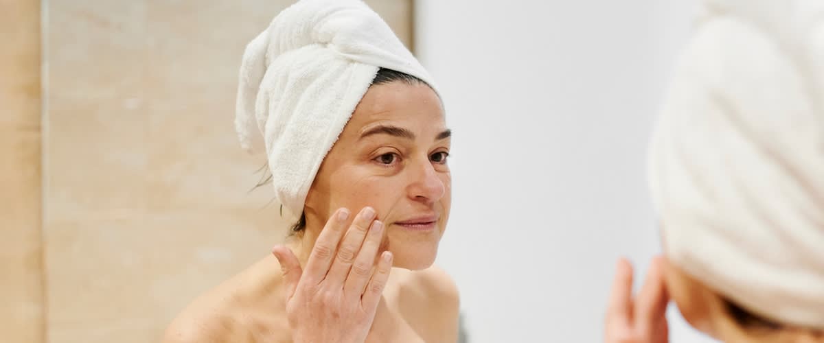 Žena s ručníkem na hlavě nanáší krém na tvář