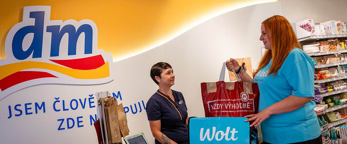 Dvě osoby v obchodě, jedna drží tašku Wolt a druhá tašku s nápisem Vždy výhodné