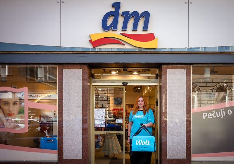 Žena s taškou Wolt stojí před obchodem dm drogerie