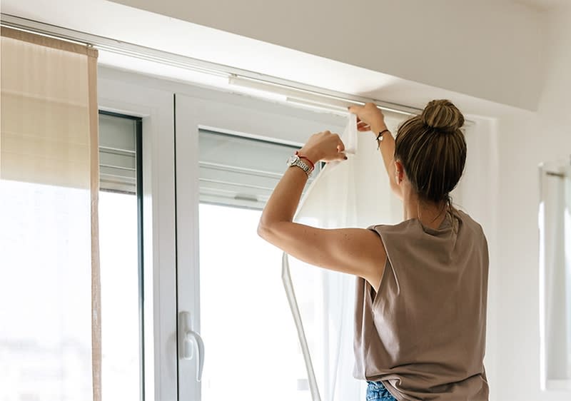 Žena montuje závěsy na okno v moderním interiéru.