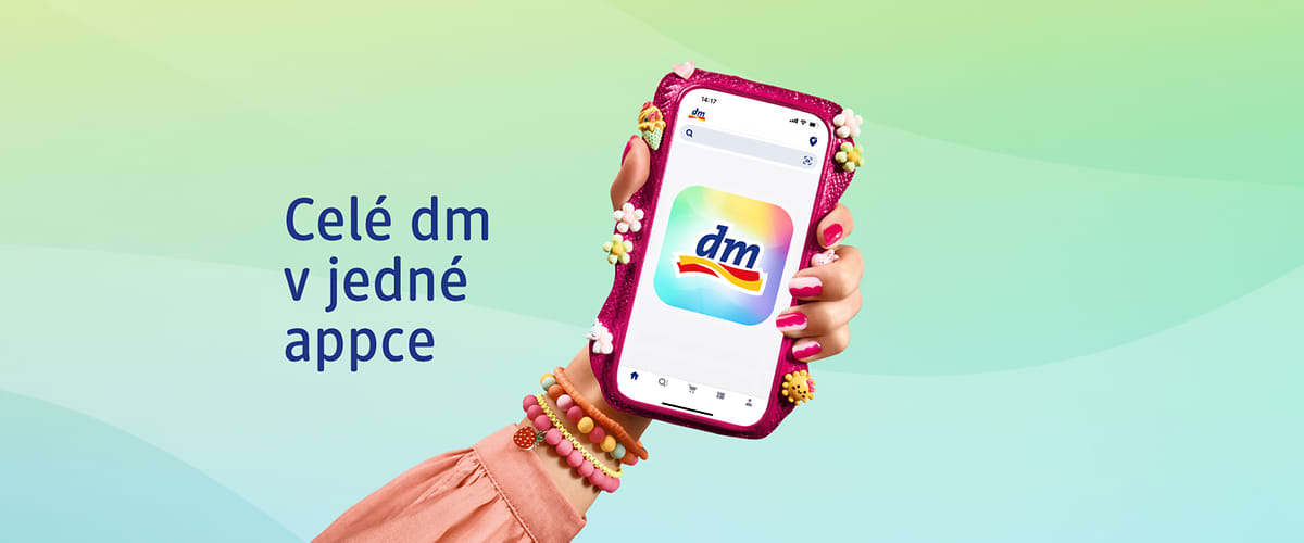 Ruka držící telefon s aplikací dm, vedle text Celé dm v jedné appce na barevném pozadí