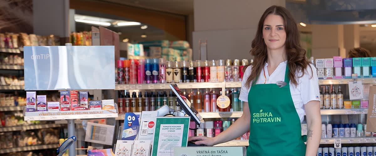 Spolupracovníčka dm v dm predajni v zelenej zástere "Sbírka potravin"
