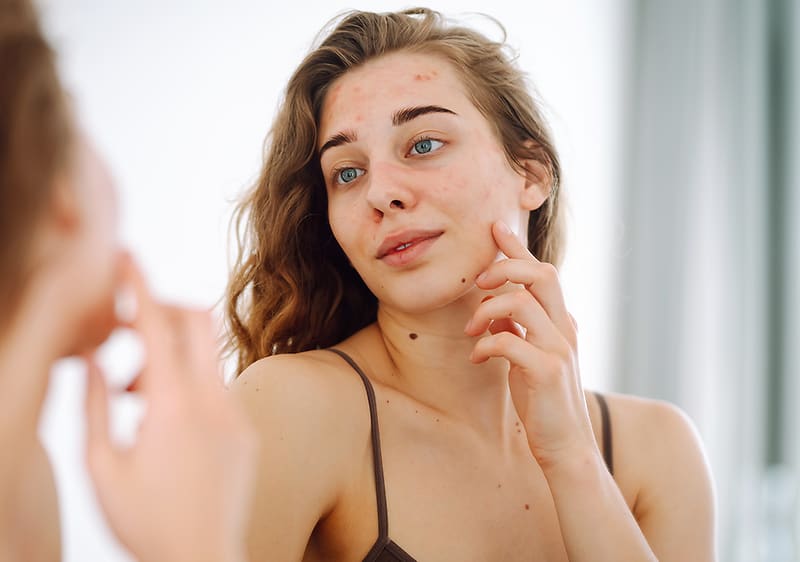 Žena s dlouhými vlasy v tílku se dívá do zrcadla