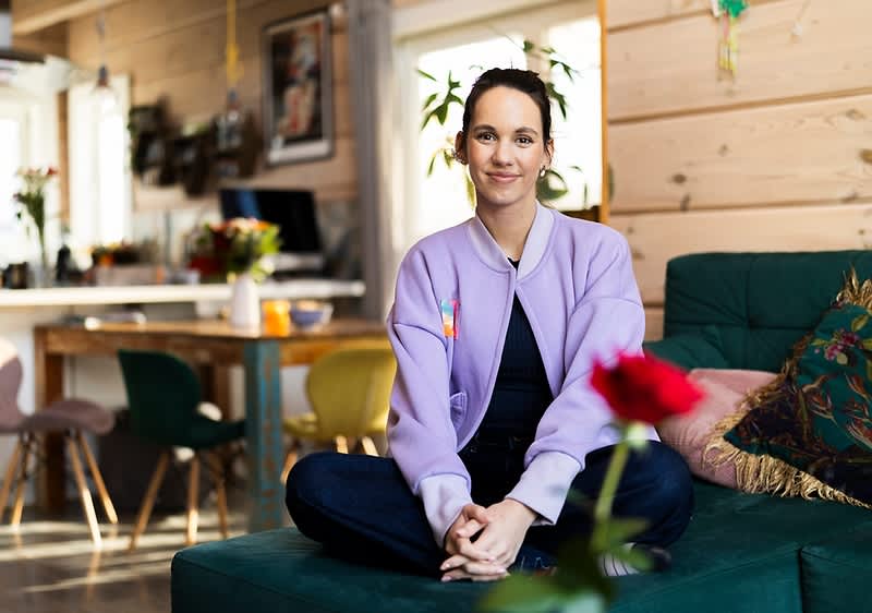 Osoba sedící na pohovce v útulném obývacím pokoji s květinou v popředí.