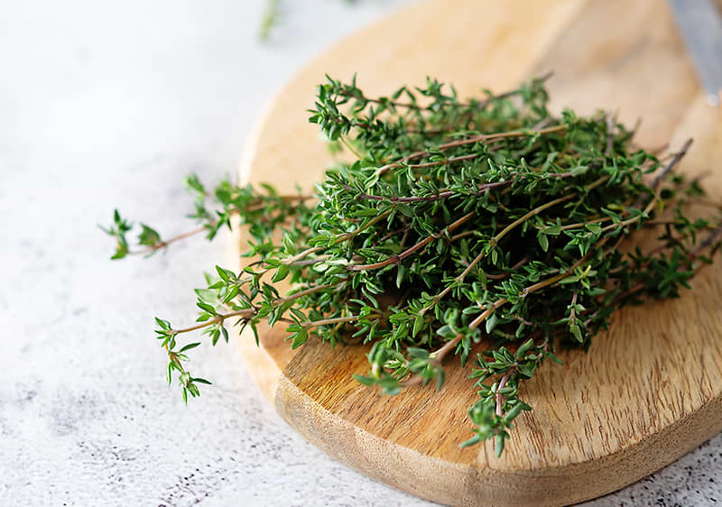 Čerstvý tymián na dřevěném prkénku na světlém povrchu