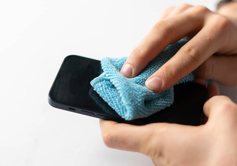 Osoba čistí mobilní telefon modrým hadříkem.