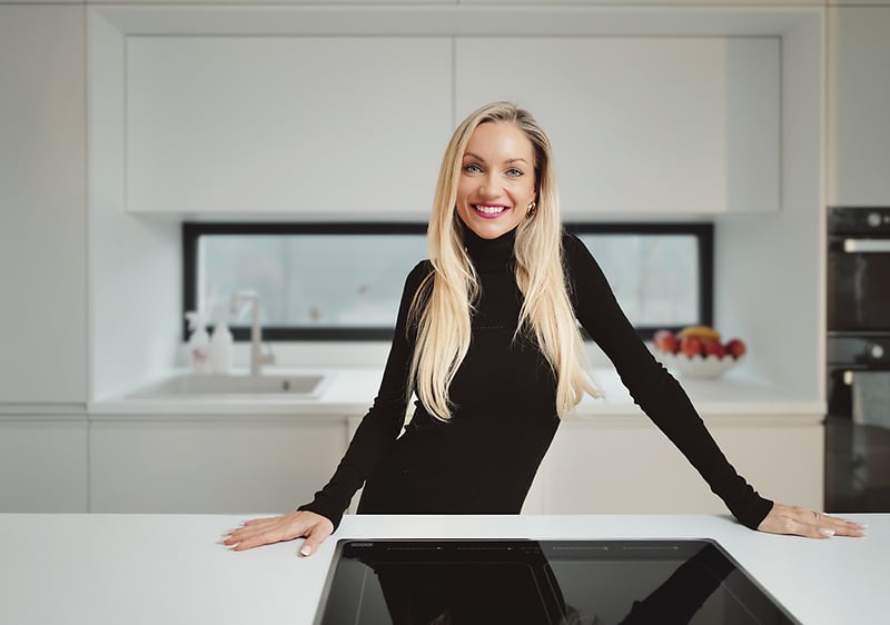 Žena stojí v moderní kuchyni, opírá se o kuchyňský pult.
