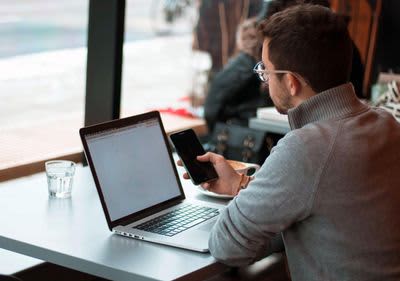 Ein Journalist sitzt in einem Kaffeehaus und wählt eine Nummer in sein Handy ein.