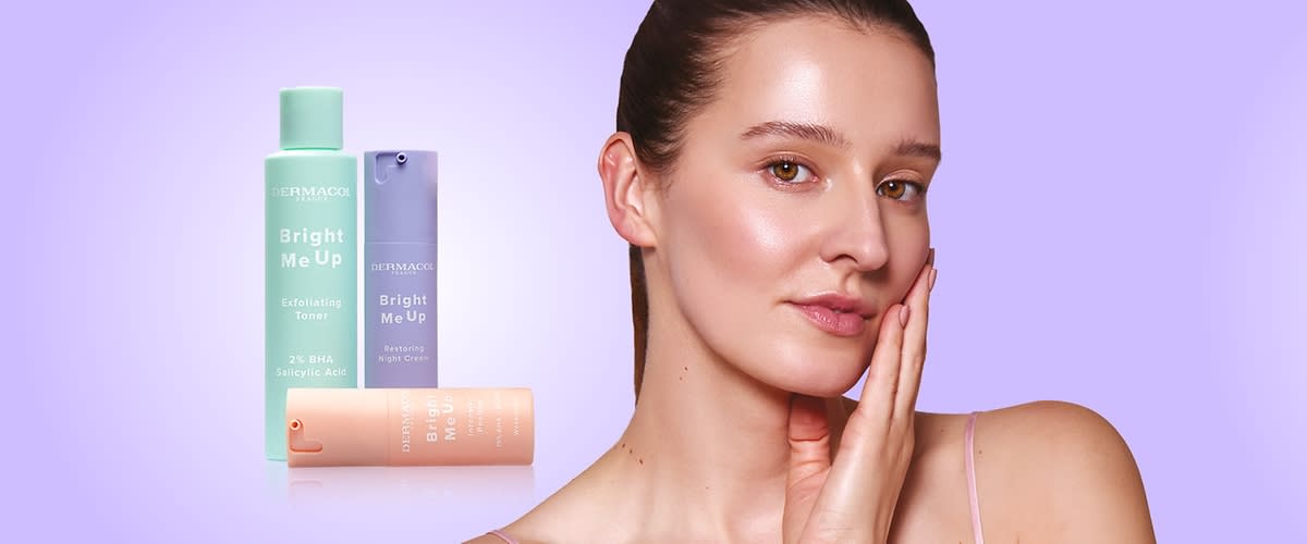 Žena s jemnou make-up tváří dotýkající se tváře vedle tří pastelových kosmetických lahviček