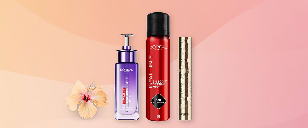 Tři kosmetické produkty L'Oréal na růžovém pozadí s květem hibisku