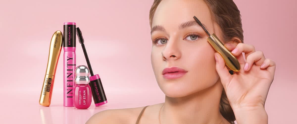 Žena s jemnou make-up tváří dotýkající se tváře vedle tří pastelových kosmetických lahviček