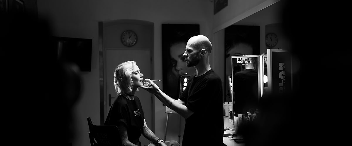 Vizážista nanáší rtěnku sedící ženě na židli v zrcadlovém make-up koutku pod studiovým světlem