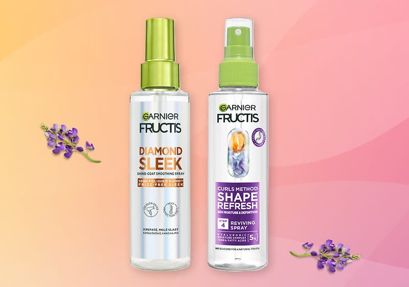Dvě průhledné plastové sprejové lahvičky Garnier Fructis vedle sebe na růžovo-oranžovém pozadí, vlevo „Diamond Sleek Shine-Coat Smoothing Spray“ s zeleným uzávěrem, vpravo „Curls Method Shape Refresh Reviving Spray“ s bílým a zeleným rozprašovačem a fialovým označením, doplněné malými květy lavandinu