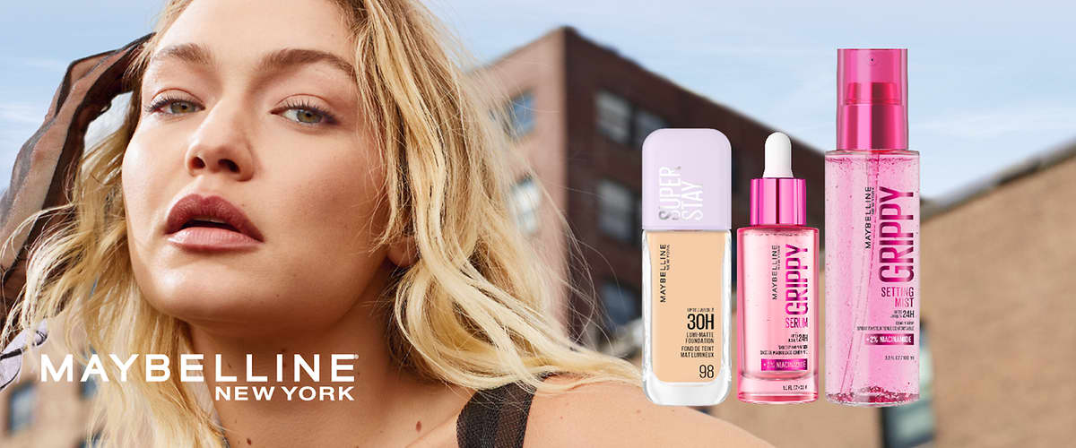 Portrét usměvavé ženy v popředí vlevo, vedle ní tři produkty Maybelline New York vpravo: krémový tekutý make-up Superstay ve světlém obalu s číslem 98, růžové sérum v lahvičce s pipetou označené „GRIPPY SERUM“ a průhledný růžový fixační sprej „GRIPPY SETTING MIST“, nápis Maybelline New York dole vlevo