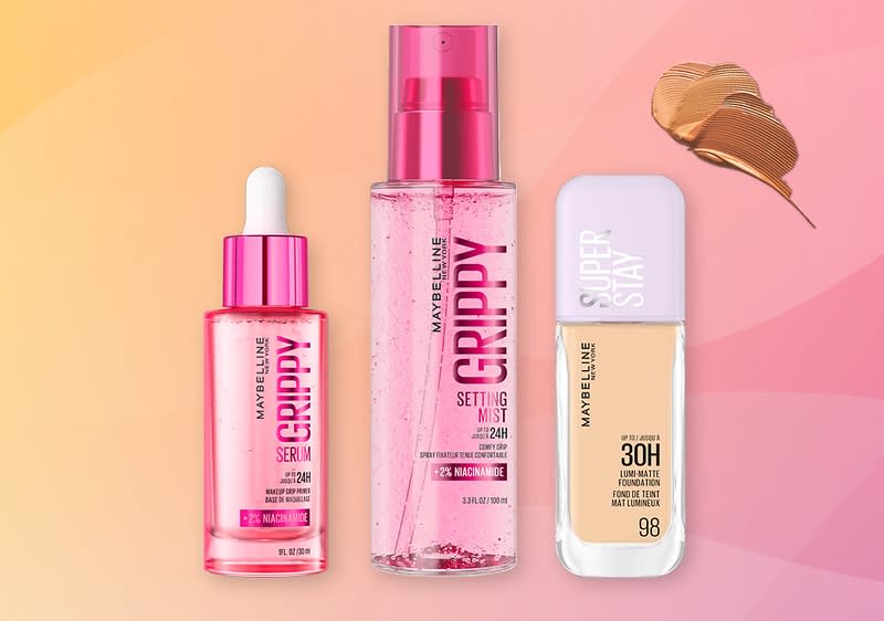 Tři kosmetické produkty značky Maybelline na růžovém pozadí: vlevo růžový skleněný kelímek séra s kapátkem a nápisem „GRIPPY SERUM“, uprostřed průhledný rozdrcený plastový sprej s nápisem „GRIPPY SETTING MIST“, vpravo světle fialové víčko a lahvička make‑upu s nápisem „SUPER STAY 30H“ a odstínem 98