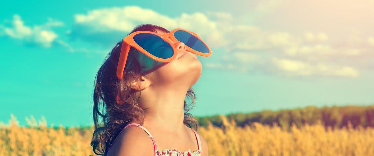 Dítě s velkými slunečními brýlemi na louce pod modrou oblohou
