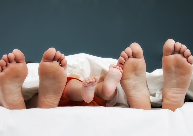 nohy dospělých a dítěte pod peřinou na posteli