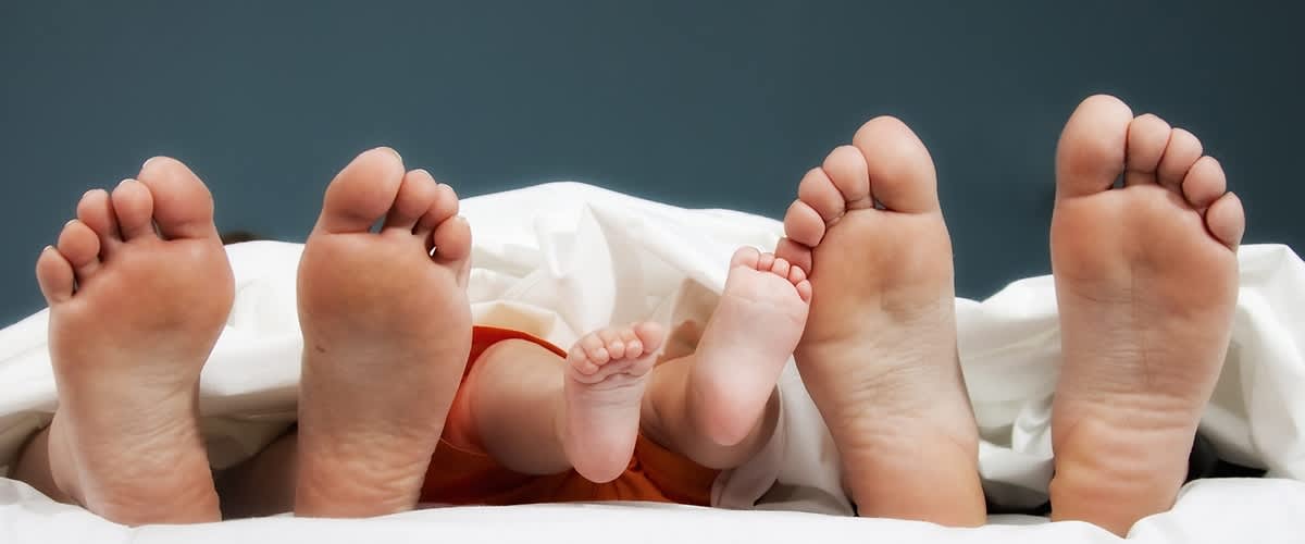 nohy dospělých a dítěte pod peřinou na posteli