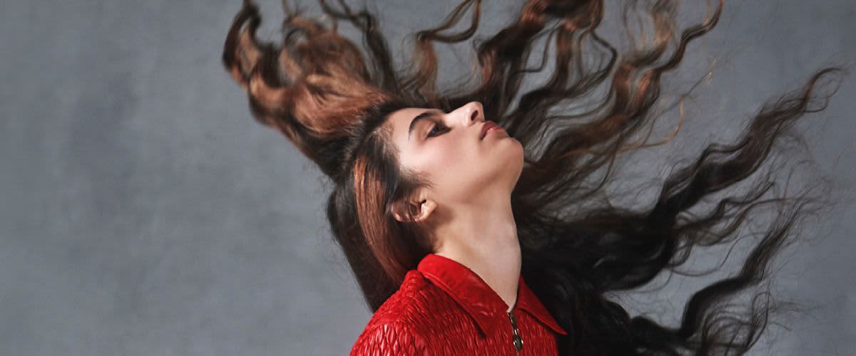 Žena v červeném s dlouhými vlasy ve vzduchu na šedém pozadí