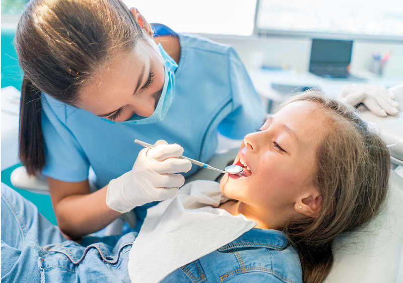 Zubařka ošetřuje pacienta v zubní ordinaci s nástrojem v ruce.